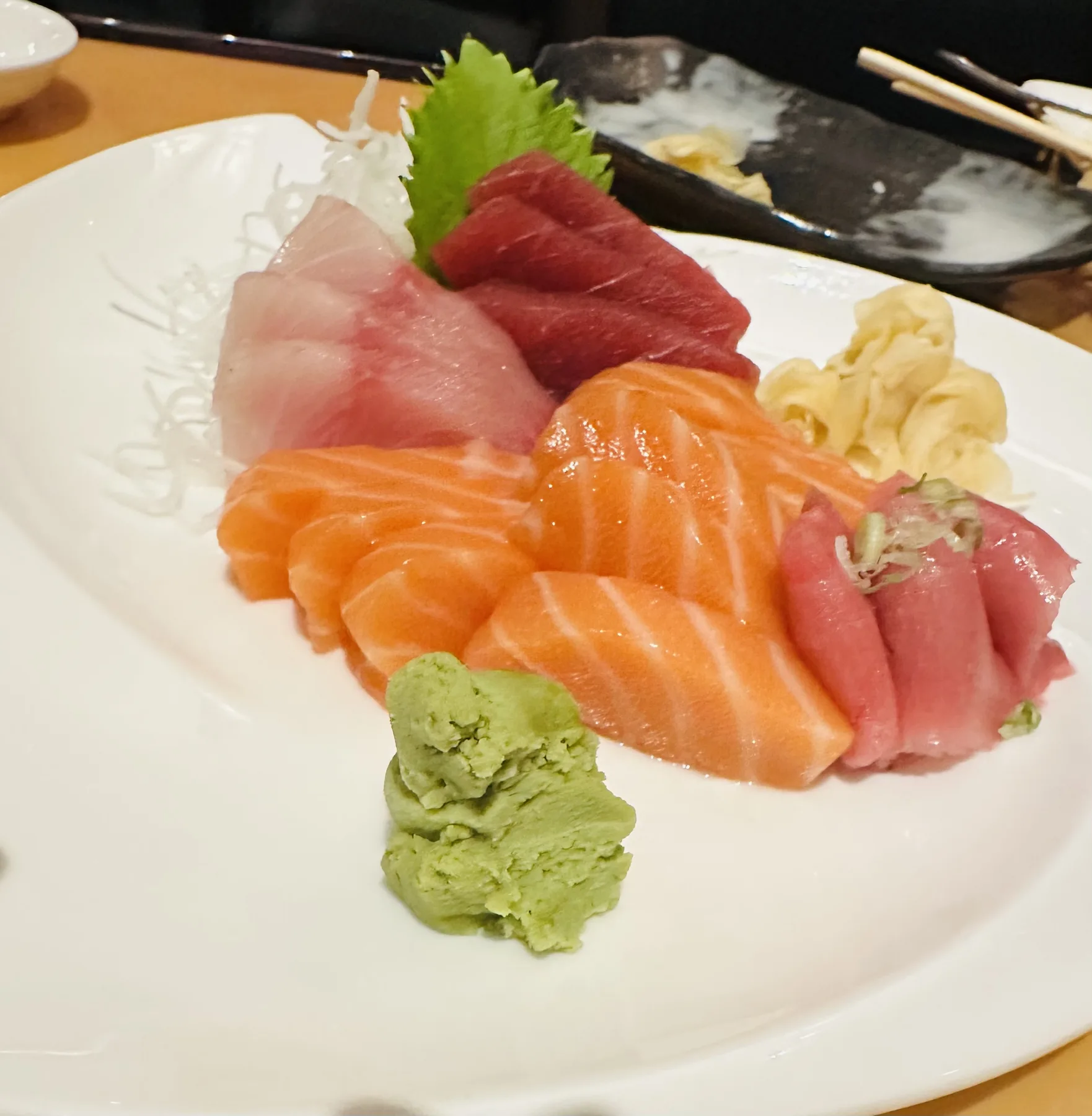 A sashimi platter at Hanami featuring salmon, tuna, and yellowtail arranged with wasabi and pickled ginger on a white ceramic plate