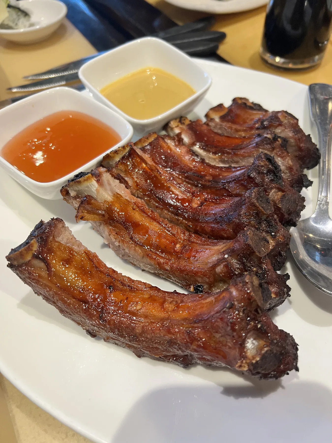 Glazed pork spare ribs with dipping sauces on a white rectangular plate