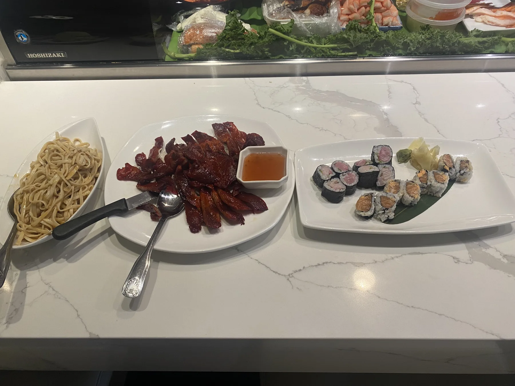Three plates including noodles, sliced meat, and sushi arranged on a marble counter