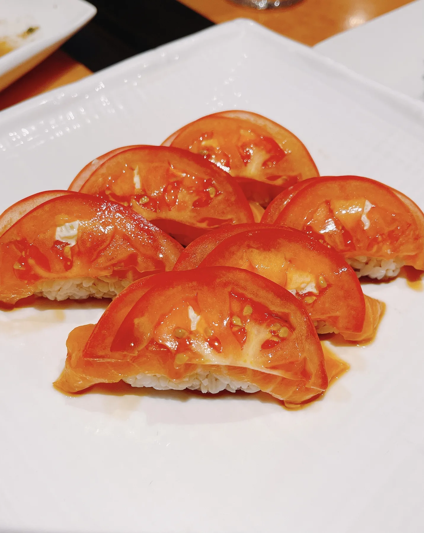Six pieces of tomato nigiri arranged on a white rectangular plate